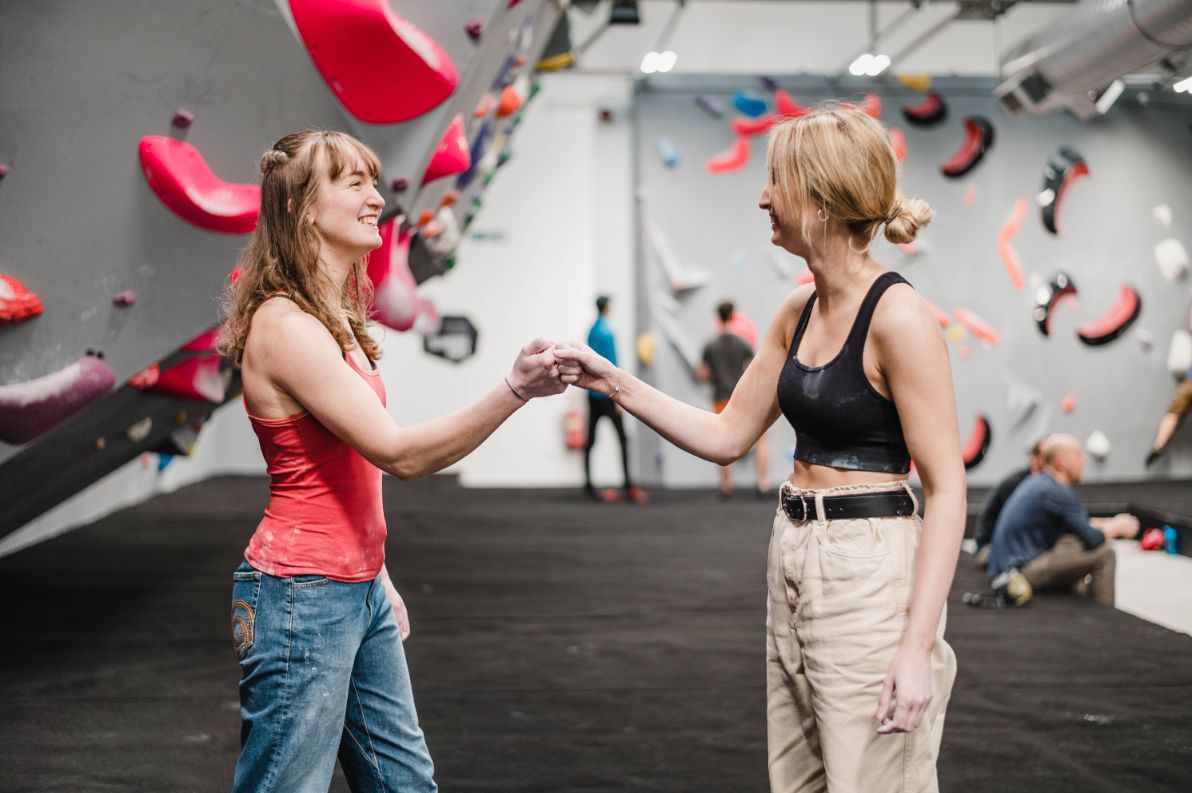 Two women fist-bumping at a climbing gym